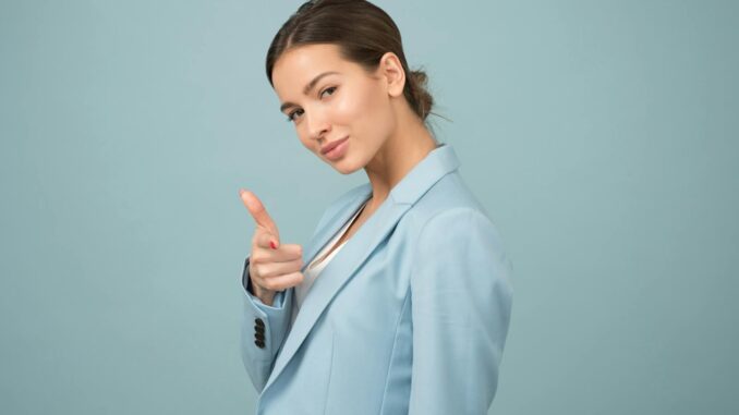 A young woman in a blue suit exhibits confidence with a relaxed pose against a blue background.