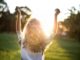 A woman with outstretched arms celebrates the sunset in a grassy field, capturing the essence of freedom and joy.